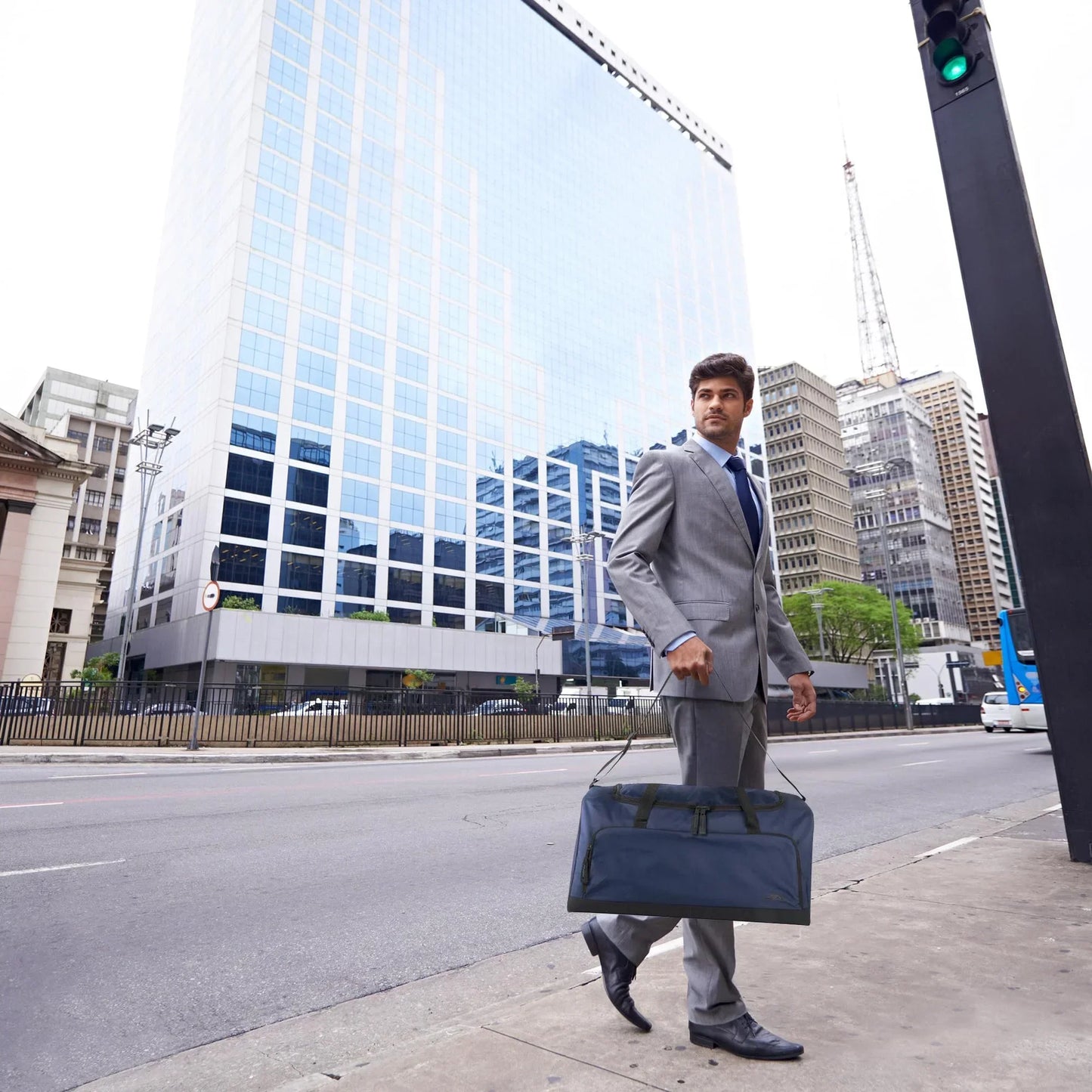 Businessman in gray suit carrying gym duffel bag on city street with modern office buildings